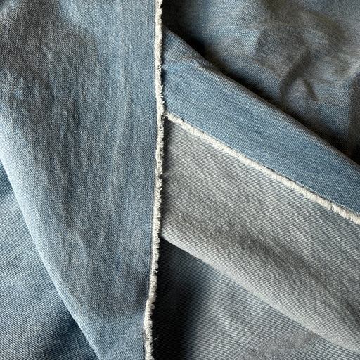 A close-up of folded light blue denim fabric showing the texture of the denim weave and a raw, frayed seam.