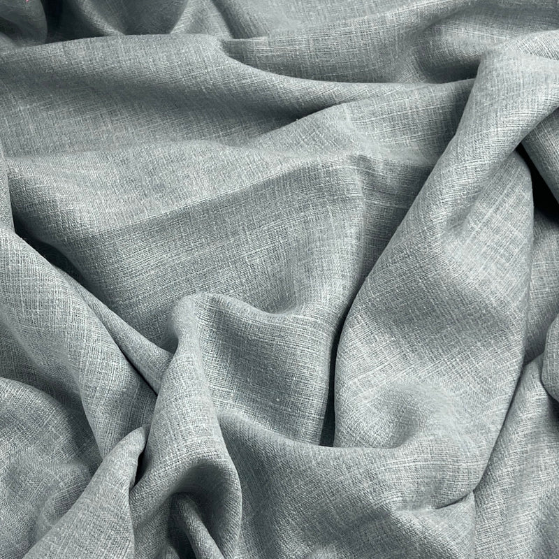 A close-up of draped light gray linen fabric with a visible woven texture and soft folds filling the frame.