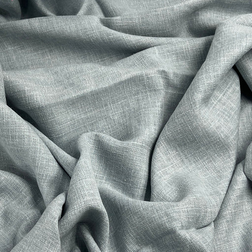 A close-up of draped light gray linen fabric with a visible woven texture and soft folds filling the frame.