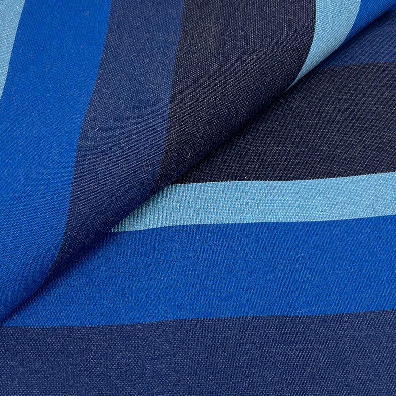 A close-up of striped fabric with horizontal bands in royal blue, navy, and light blue, shown with a folded corner revealing the woven texture.