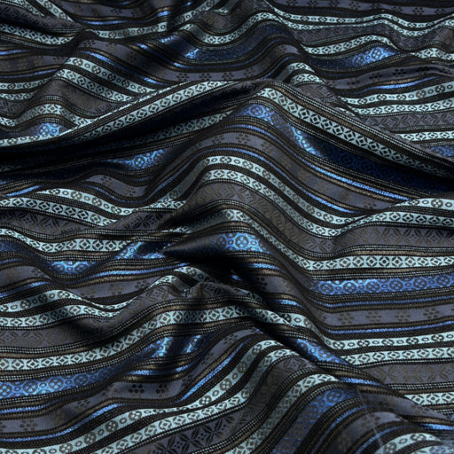 A close-up of a draped fabric with a dark charcoal base and horizontal stripes in metallic blue, light blue, and silver with geometric patterns.
