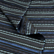 A close-up of patterned fabric with horizontal woven stripes in black, dark brown, blue, and off-white, shown with a folded corner revealing the texture.