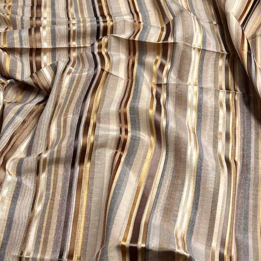 A close-up of draped fabric with vertical stripes in beige, brown, gray, and metallic gold tones.
