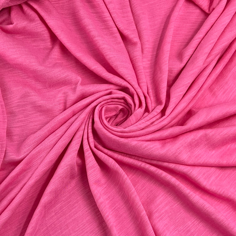 A close-up of draped pink fabric arranged in a spiral pattern, showing its soft texture and folds.