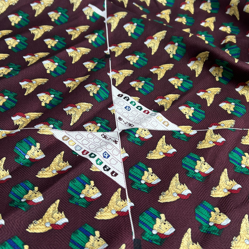 A close-up of patterned fabric with a dark burgundy background, repeating gold bird motifs, green plaid shapes, and a white star-shaped patchwork section with small colored squares.