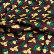 A close-up of draped fabric with a repeating holiday print featuring yellow puppies wearing red Santa hats and green plaid outfits on a dark brown background.