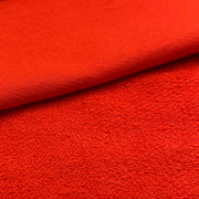 A close-up of bright red textured fabric, showing a folded corner that reveals the knit or terry-like surface detail.
