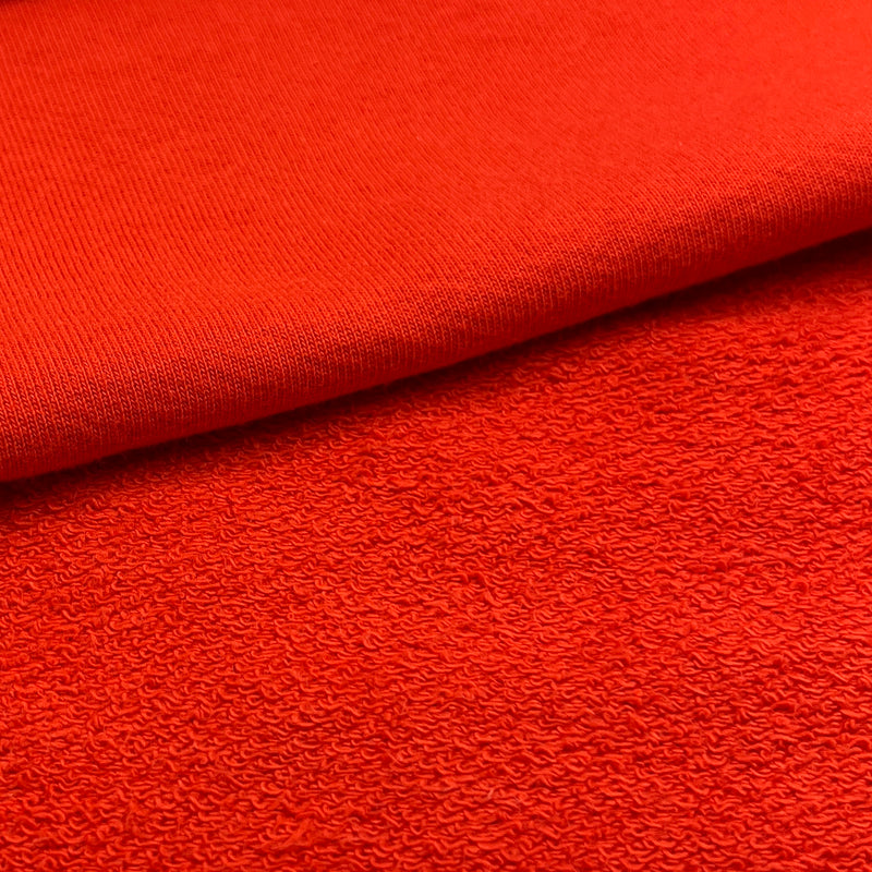 A close-up of bright red textured fabric, showing a folded corner that reveals the knit or terry-like surface detail.