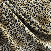 Leopard print fabric draped in soft folds, showing a classic animal spot pattern in black, brown, and beige on a cream background.