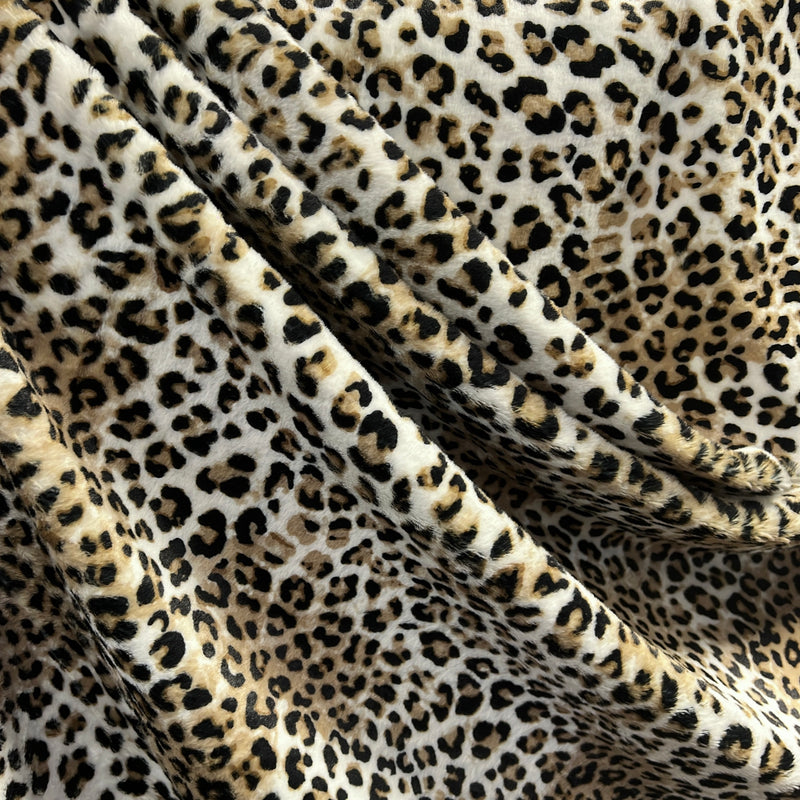 Leopard print fabric draped in soft folds, showing a classic animal spot pattern in black, brown, and beige on a cream background.
