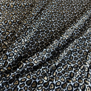 Leopard print fabric with black, brown, and beige spots on a white background, shown with soft folds.