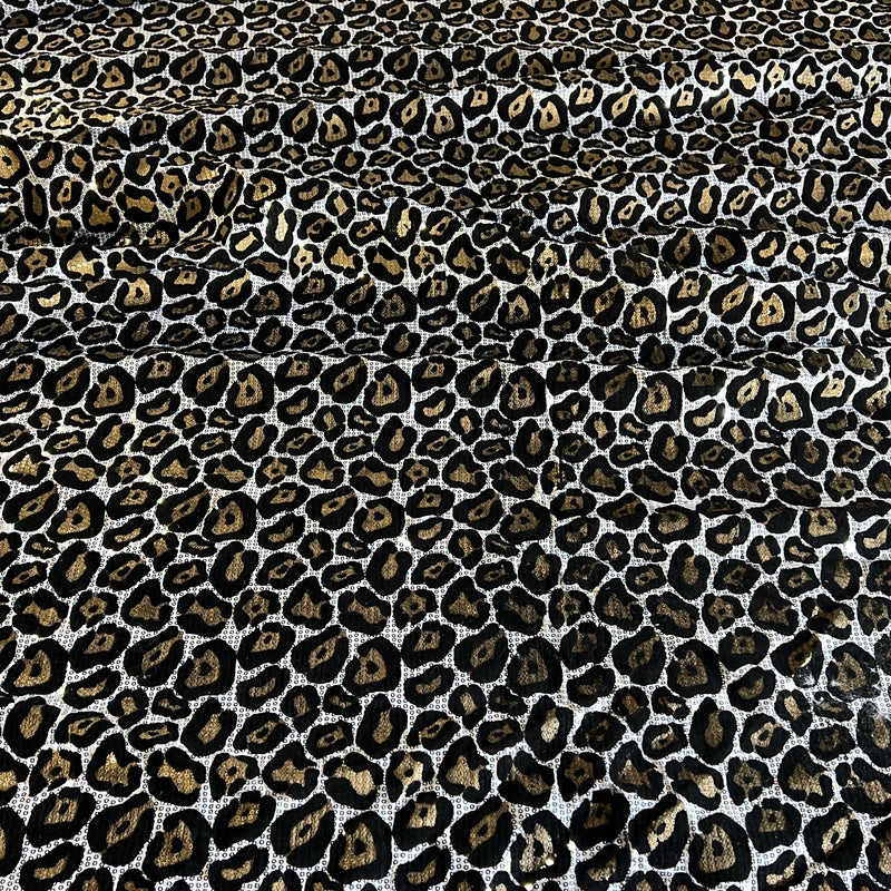 Leopard print fabric with black, brown, and beige spots on a white background, shown as a close-up texture.