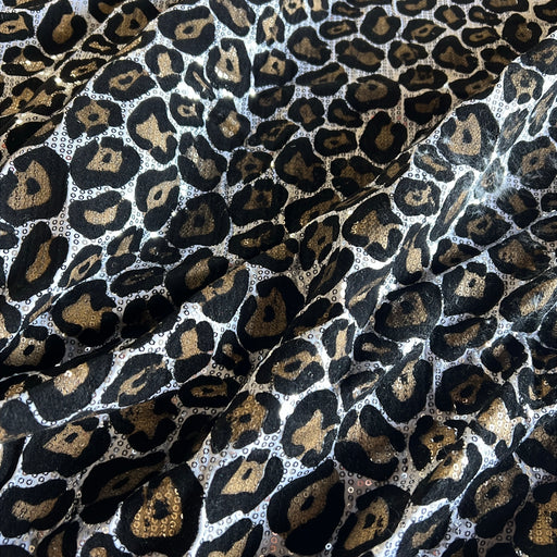 Leopard print fabric with black, brown, and gold spots on a white base, shown in soft folds.