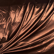 A close-up of draped metallic copper-brown fabric with a satin-like sheen and soft folds.