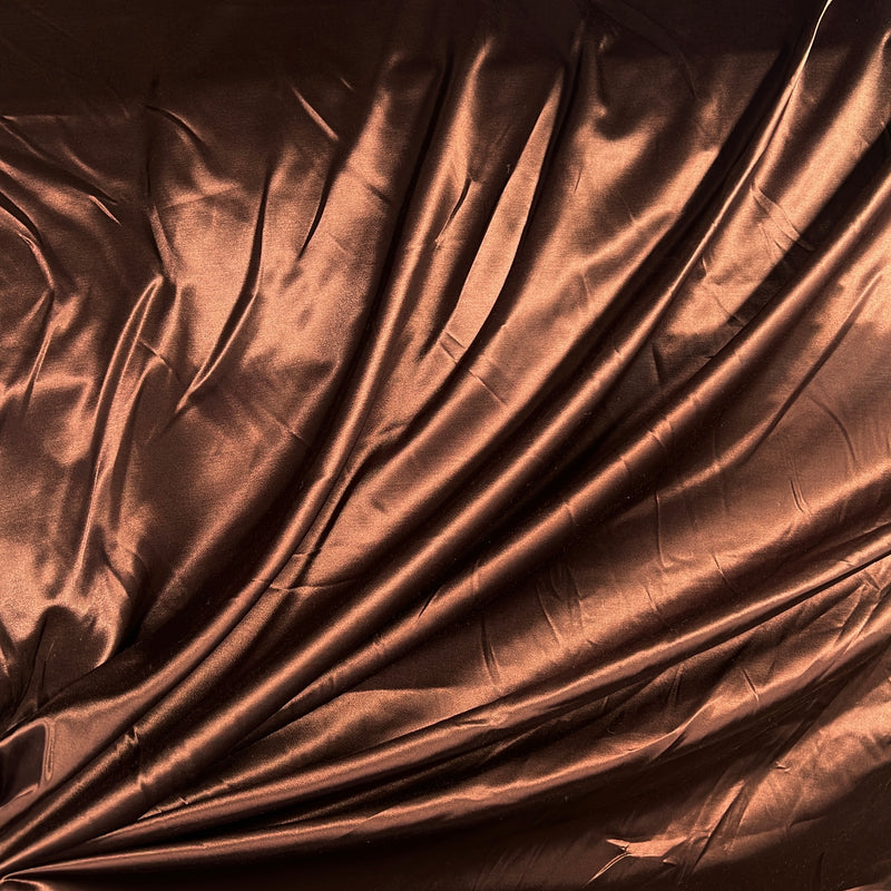 A close-up of draped metallic copper-brown fabric with a satin-like sheen and soft folds.