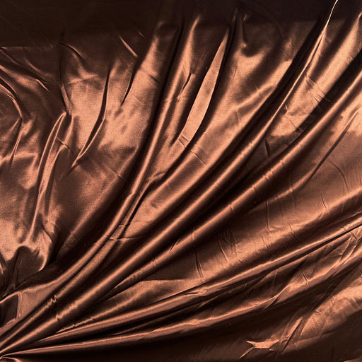 A close-up of draped metallic copper-brown fabric with a satin-like sheen and soft folds.
