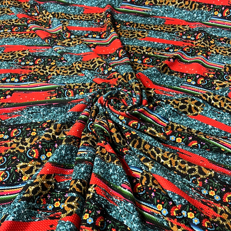 A close-up of a draped fabric with a complex multicolor pattern featuring leopard print, red stripes, and small floral motifs.