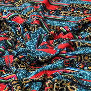 A close-up of a draped, highly patterned fabric featuring a mix of leopard print, blue glitter, red stripes, and colorful floral motifs.