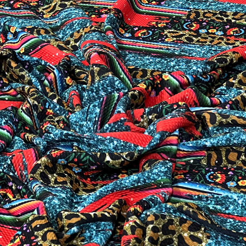 A close-up of a draped, highly patterned fabric featuring a mix of leopard print, blue glitter, red stripes, and colorful floral motifs.