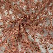 Rose gold sequin lace fabric draped in a spiral pattern, showing intricate floral lace details covered in shimmering rose gold sequins and glitter.
