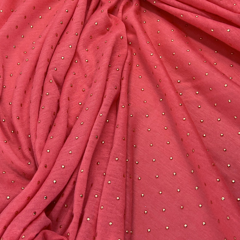 A close-up of draped dusty rose pink fabric with small metallic silver rhinestone dots scattered across it.