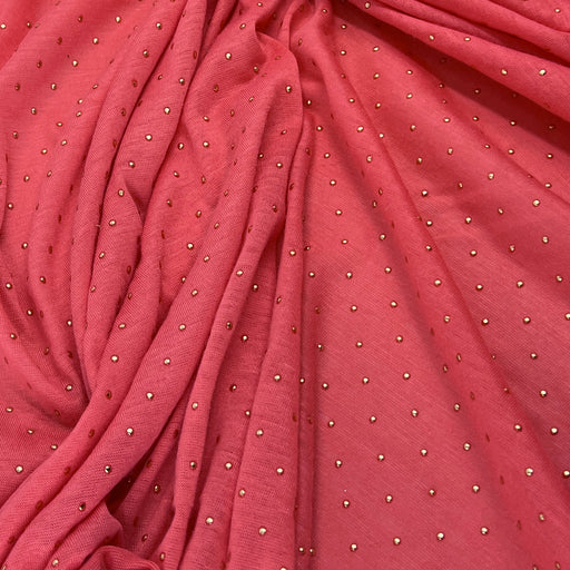 A close-up of draped dusty rose pink fabric with small metallic silver rhinestone dots scattered across it.