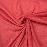 A close-up of coral pink fabric arranged in a spiral drape, featuring a repeating pattern of small metallic silver dots.