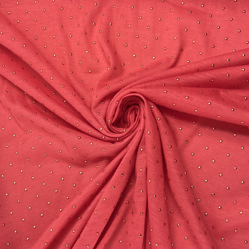 A close-up of coral pink fabric arranged in a spiral drape, featuring a repeating pattern of small metallic silver dots.