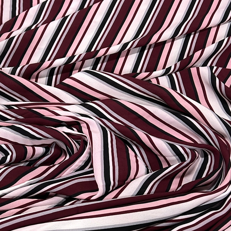 A close-up of draped striped fabric with alternating diagonal bands of burgundy, light pink, white, and black.