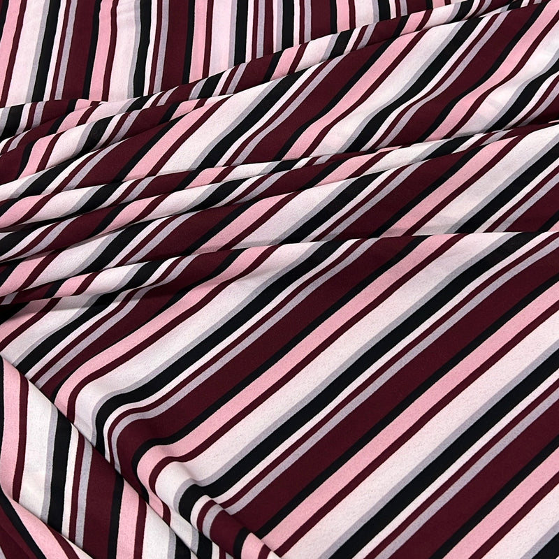 A close-up of draped striped fabric with diagonal bands in burgundy, pink, white, and black.