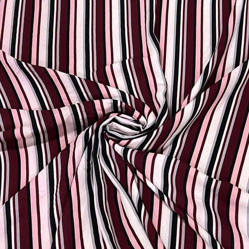 A close-up of striped fabric arranged in a spiral drape, showing alternating vertical stripes in burgundy, light pink, white, and black.