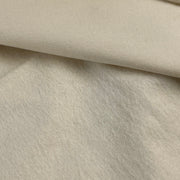 A close-up of a soft, textured fabric in a warm off-white or cream color, folded to show its ribbed and plush surface.