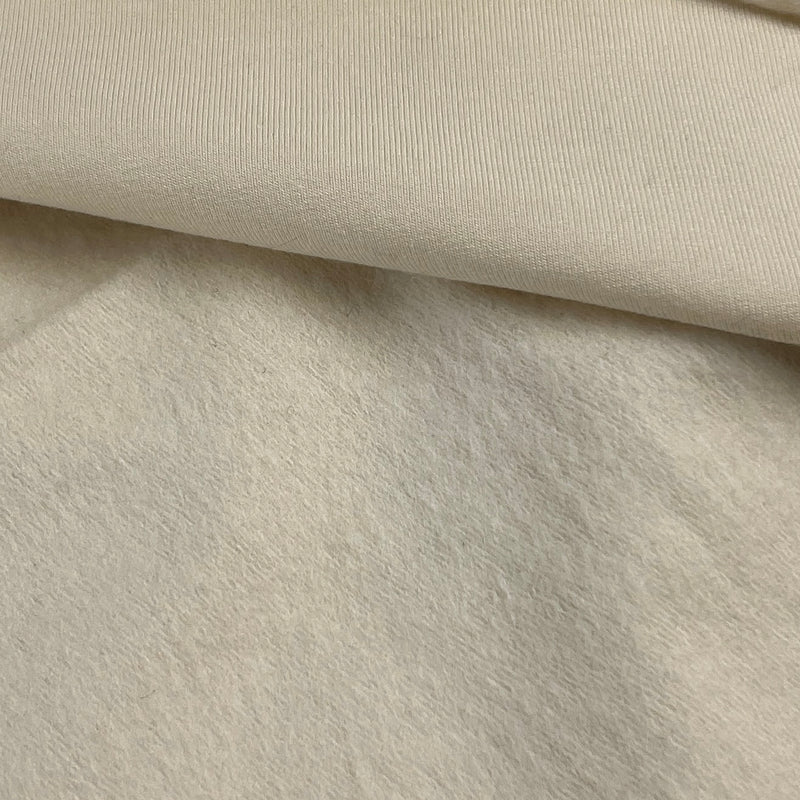 A close-up of a soft, textured fabric in a warm off-white or cream color, folded to show its ribbed and plush surface.