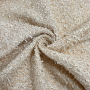 A close-up of a textured fabric with a shaggy, curly surface in warm off-white and beige tones, arranged in a spiral drape.