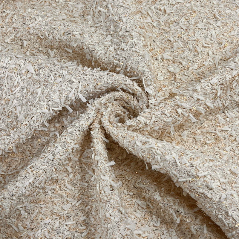 A close-up of a textured fabric with a shaggy, curly surface in warm off-white and beige tones, arranged in a spiral drape.
