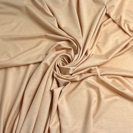 A close-up of draped beige fabric arranged in a spiral, showing its smooth texture and soft sheen.