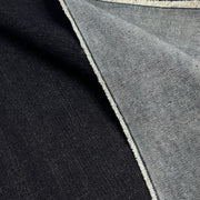 Close-up of a folded textile showing two fabric colors: a very dark indigo side and lighter reverse, emphasizing the broken twill weave.