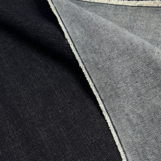 Close-up of a folded textile showing two fabric colors: a very dark indigo side and lighter reverse, emphasizing the broken twill weave.
