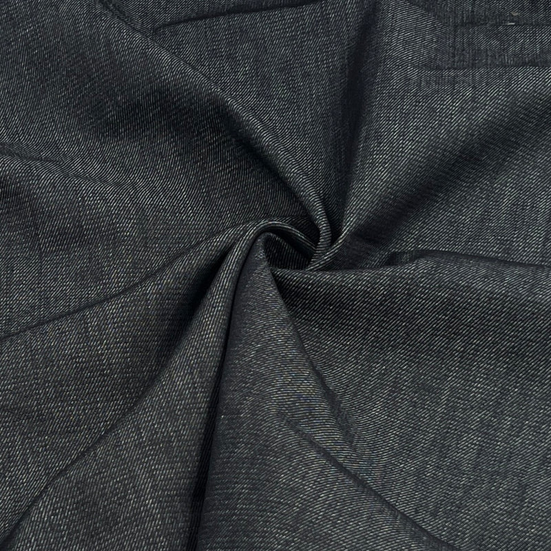 A close-up of dark indigo denim fabric, gathered in the center to show its weave and drape.