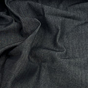 A close-up of dark dark indigo denim fabric with a textured twill-like weave, shown in soft folds.