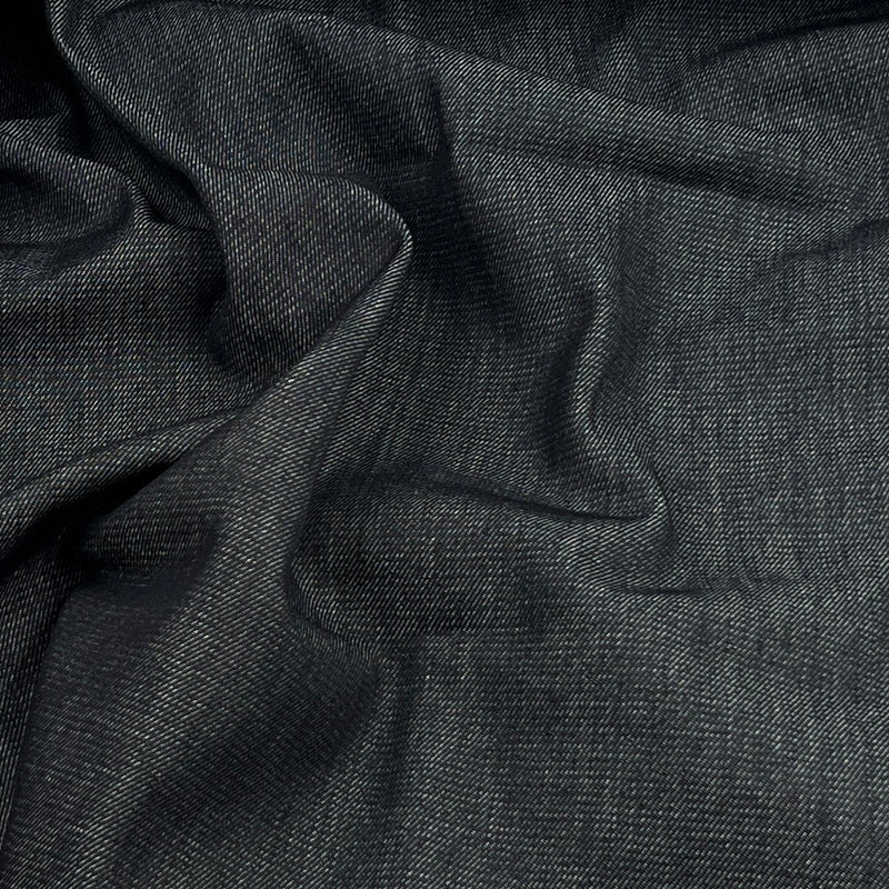 A close-up of dark dark indigo denim fabric with a textured twill-like weave, shown in soft folds.