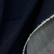 Close-up of dark indigo blue denim fabric with a visible white frayed cut edge and a lighter gray-blue woven underside.