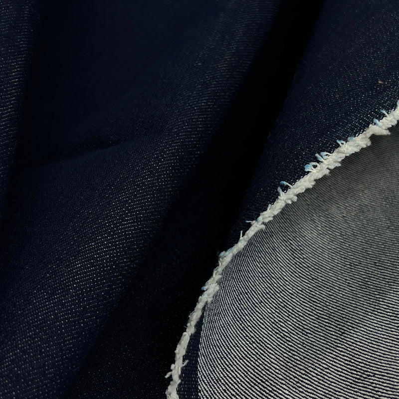 Close-up of dark indigo blue denim fabric with a visible white frayed cut edge and a lighter gray-blue woven underside.