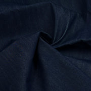 A close-up of dark indigo blue fabric with a subtle woven texture, gathered in soft folds.