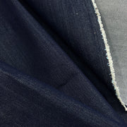 A close-up of dark indigo blue denim fabric with a visible white frayed edge showing the lighter inner weave.