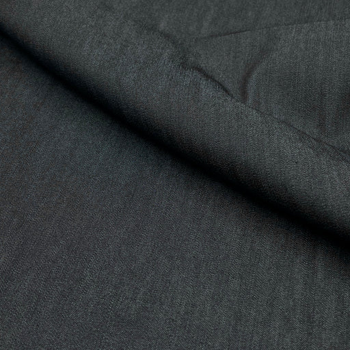 A close-up of dark charcoal gray textured fabric with a diagonal fold showing the material's fine weave.