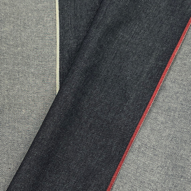 Close-up of folded dark indigo denim fabric with a thin red stitched edge, layered over lighter gray reverse.