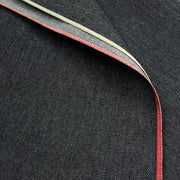 Close-up of dark indigo denim fabric with a folded corner revealing a red and cream-colored herringbone contrast edge.