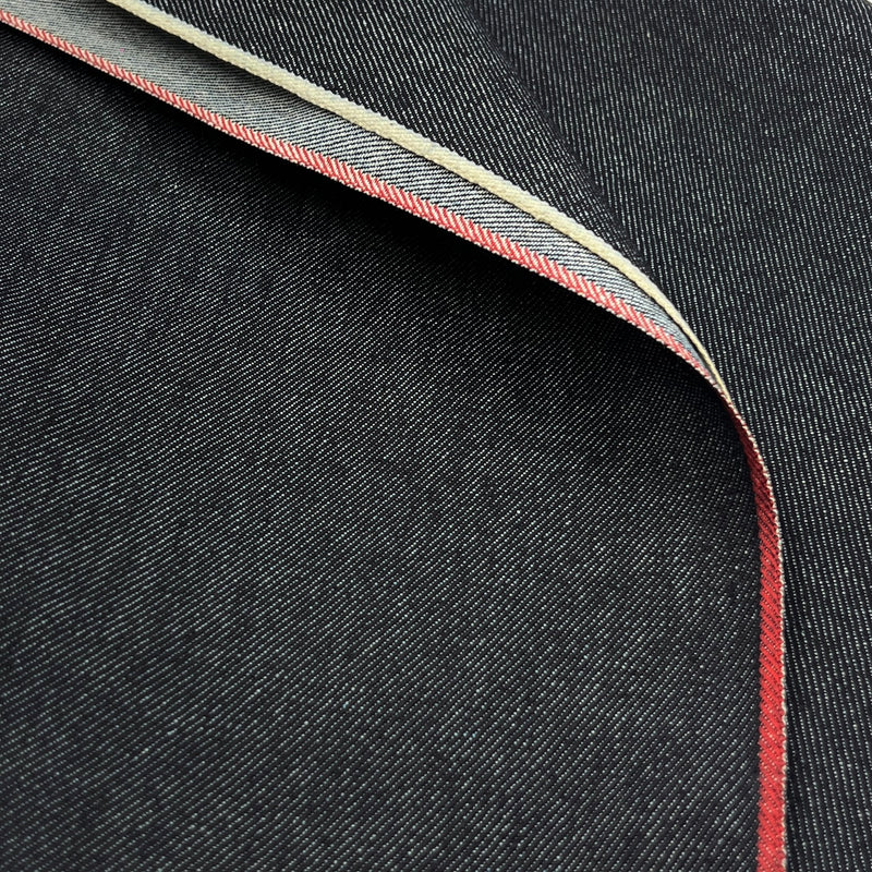 Close-up of dark indigo denim fabric with a folded corner revealing a red and cream-colored herringbone contrast edge.