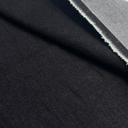 A close-up of black fabric with a visible woven texture and a folded edge showing a lighter gray underside.